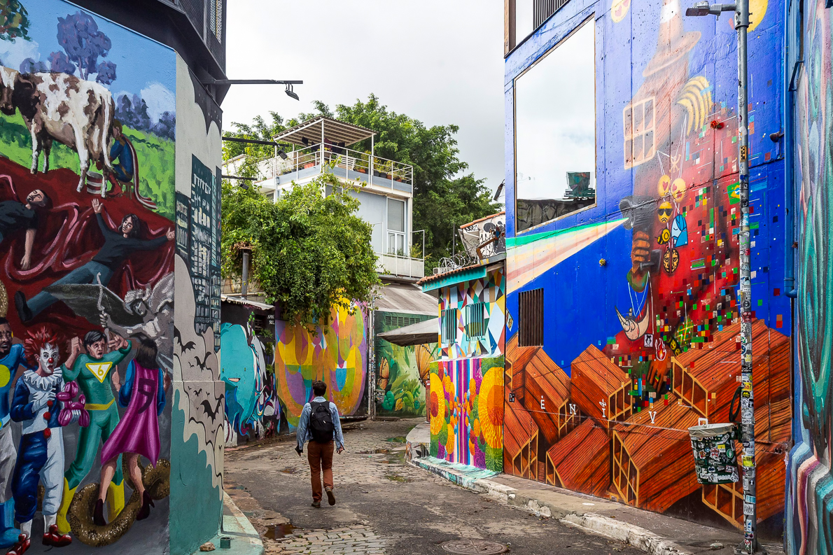 Turista recorriendo el Beco do Batman en São Paulo, callejón de Vila Madalena con murales de arte urbano y graffitis coloridos, popular entre viajeros LGBT